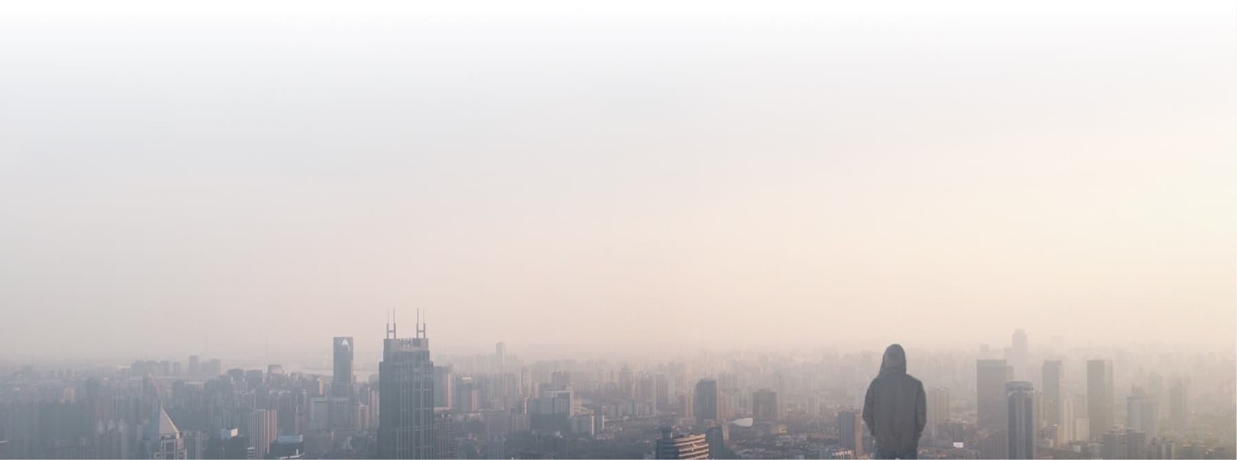 Man in hooded sweatshirt overlooking smoggy cityscape