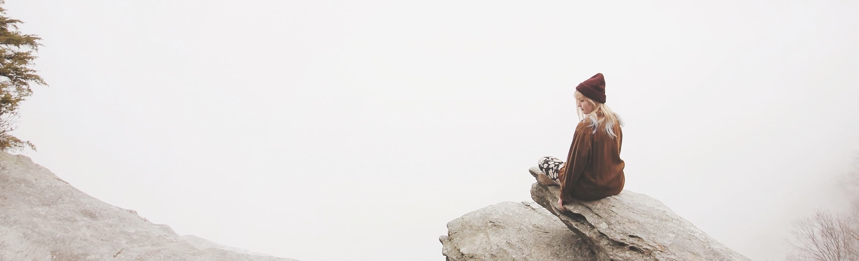 Woman sitting on edge of rock overlooking foggy landscape